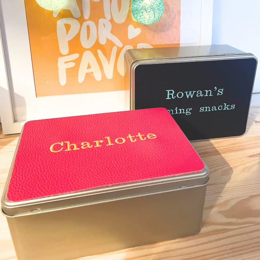 Personalised tins with custom names, one red with 'Charlotte', one black with 'Rowan’s gaming snacks'.