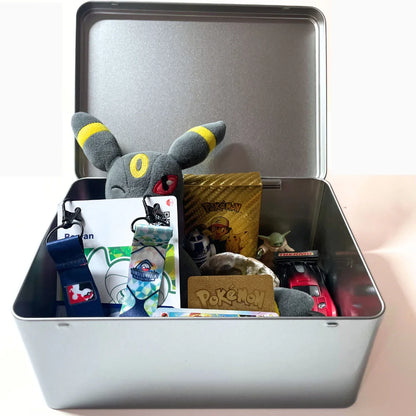 Open keepsake tin with Umbreon plush, Pokémon cards, lanyards, toy car, and collectibles
