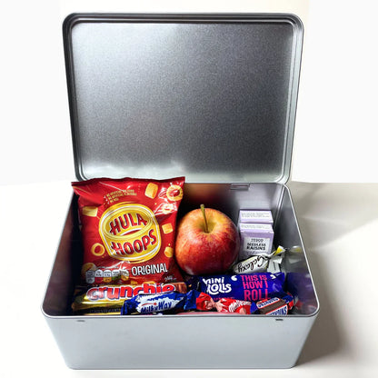 Open metal snacks tin with Hula Hoops crisps, apple, raisins, and assorted chocolates