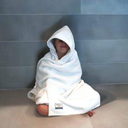 Child wrapped up in a  large hooded towel sitting on the bathroom floor